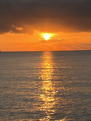 The sun rising out of the Mediterranean under a dark band of cloud, its reflection a gold stripe across the water