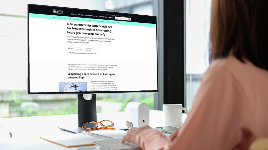 A woman working at a computer showing the front-end of the new Announcement content type on the screen. The updated design with the Navigation section and supporting imagery are visible.