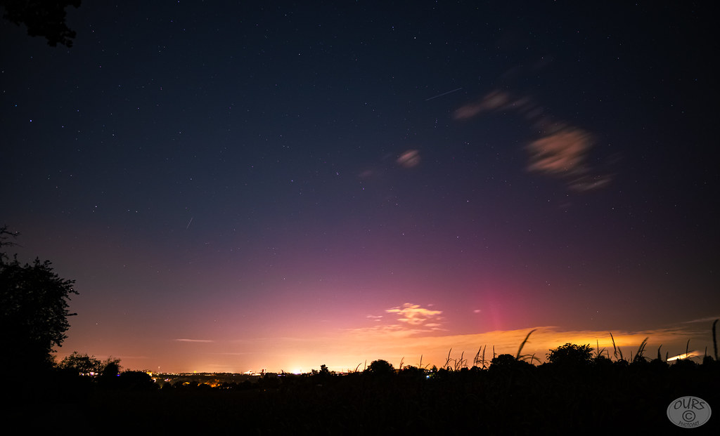 Ciel nocturne étoilé avec une lueur rose et pourpre au-dessus de l'horizon nord, sous la lumière orange d'une ville.