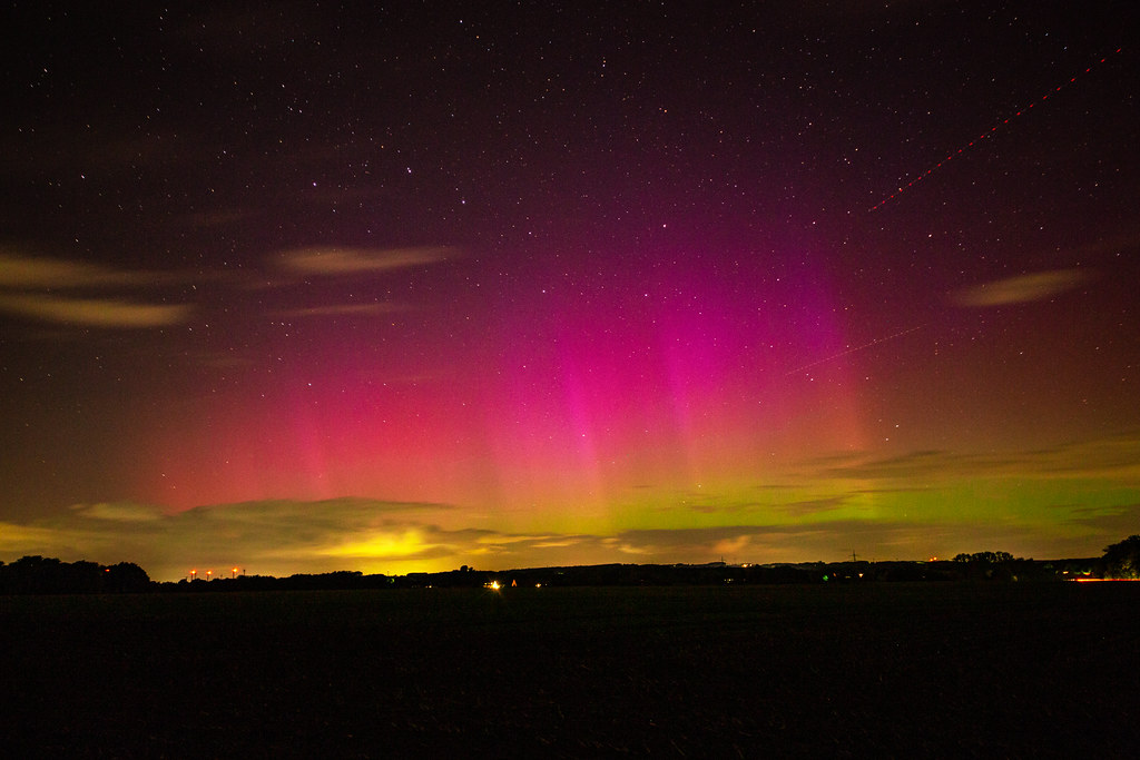 Colonnes d'aurore roses et magenta au-dessus d'un champ, avec une bande verte à l'horizon et des étoiles.