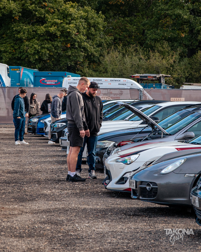 Car enthusiasts talking beside a line of parked cars at a Takona car meet