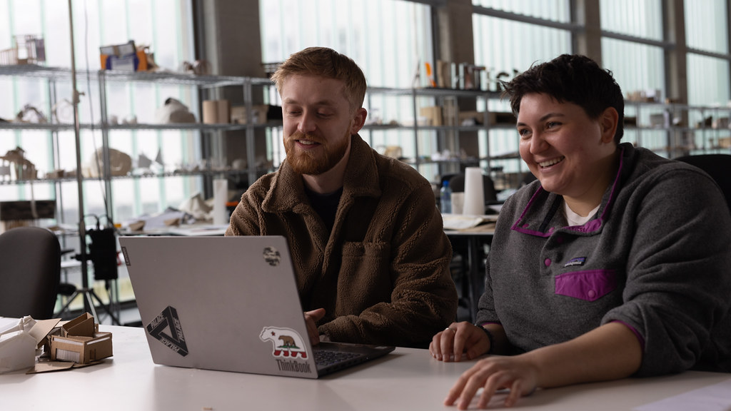 Two students sit at desk in design studio with laptop
