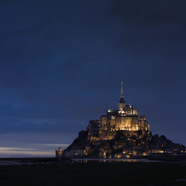 mont saint michel fully lit for the night, as the sunset fades in the west.