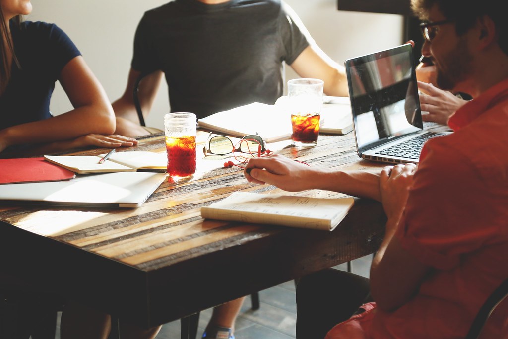 A small team working through notes and laptops around a shared table — photo by ChristopherA, CC0, via Openverse
