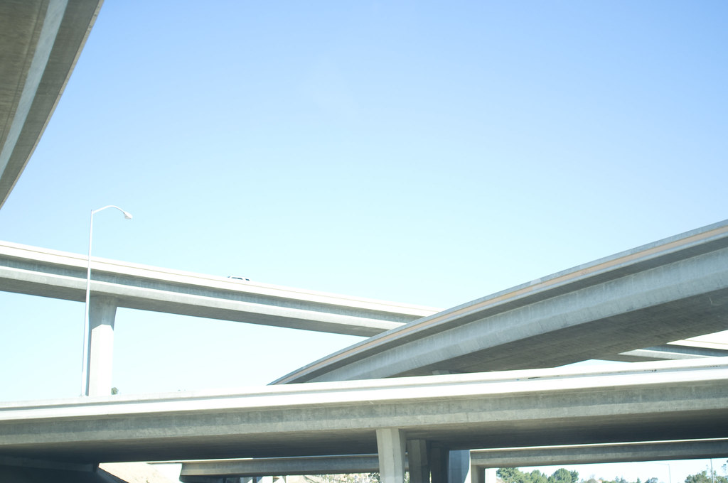 Low-angle view of massive curved concrete highway flyover overpasses soaring against an open blue California sky.
