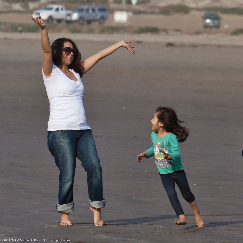 Running circles on the beach, young female child circles her mother who is holding her welcoming arms out.