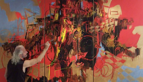 Artist reaching up to work on a large red painting