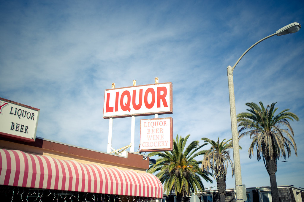 Vintage roadside sign reading 'LIQUOR' and 'LIQUOR BEER WINE GROCERY' with palms against a blue sky.