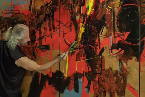Artist holding a brush before a red abstract painting