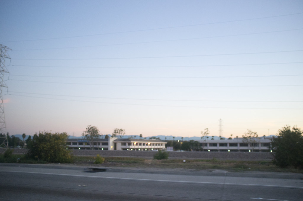 Hazy twilight view across a highway toward low-rise buildings and transmission towers in California.