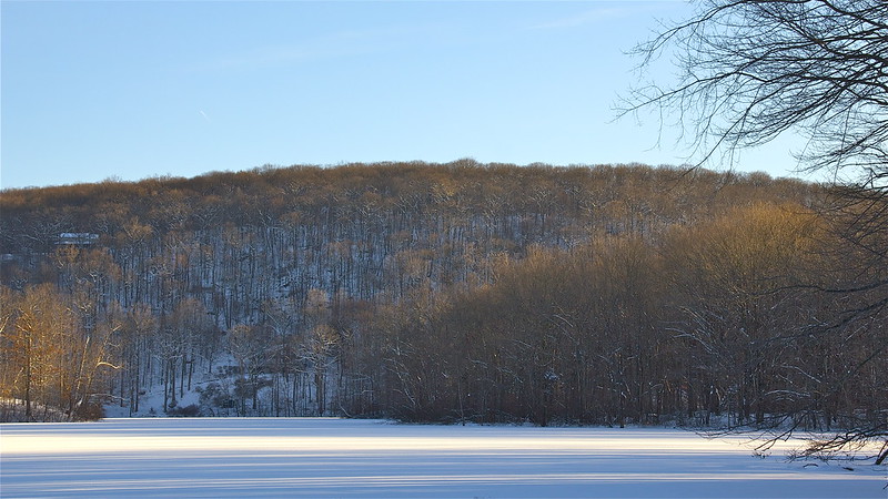 Frozen Pierrepont Lake below a wooded hill
