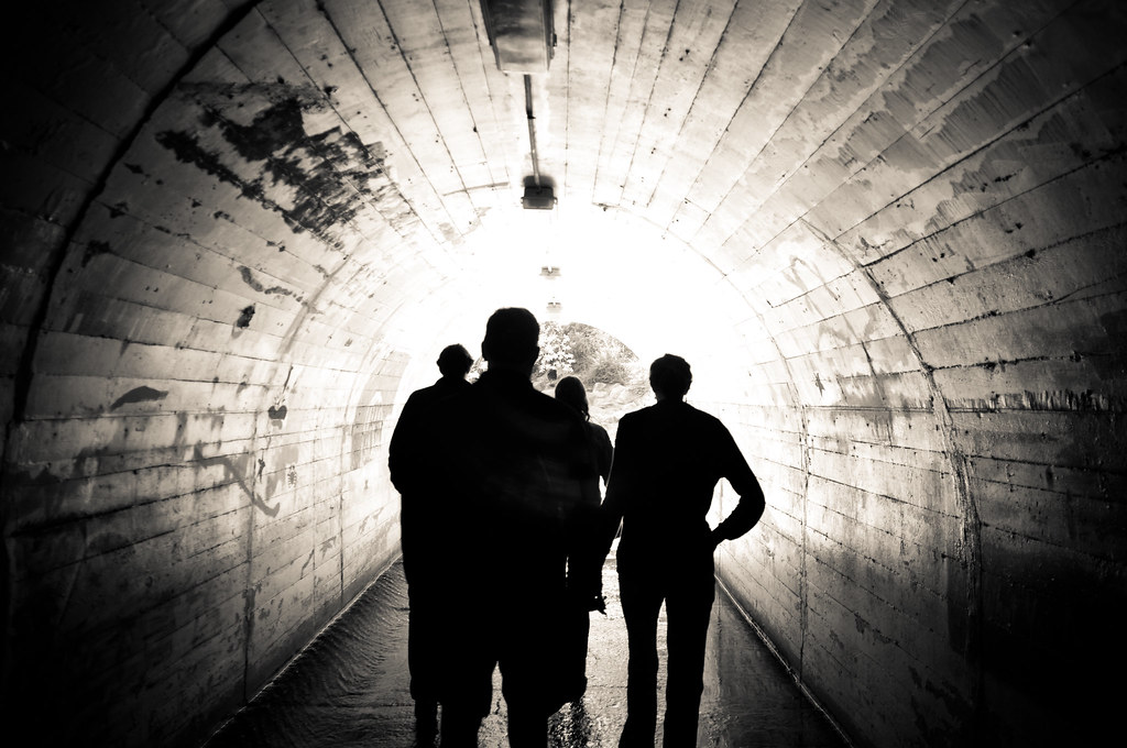 Silhouettes of people walking through an arched concrete pedestrian underpass toward daylight in California.