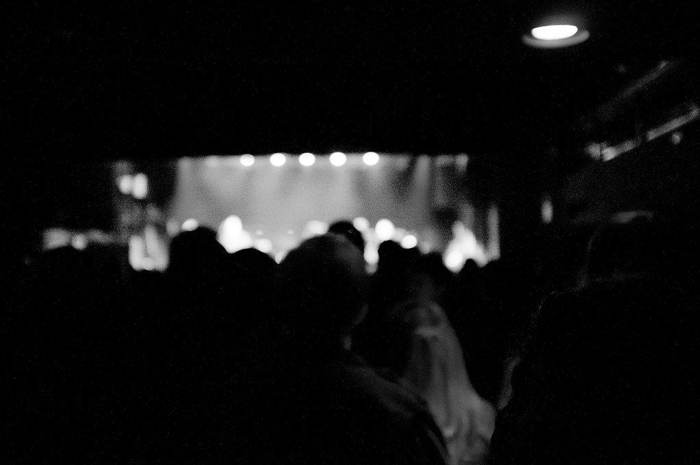 Black and white concert view from a dark crowd looking toward an illuminated stage in a New York City venue.