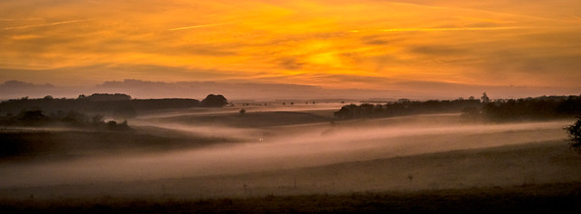 A car drives through the evening mist on Salisbury Plain in Wiltshire