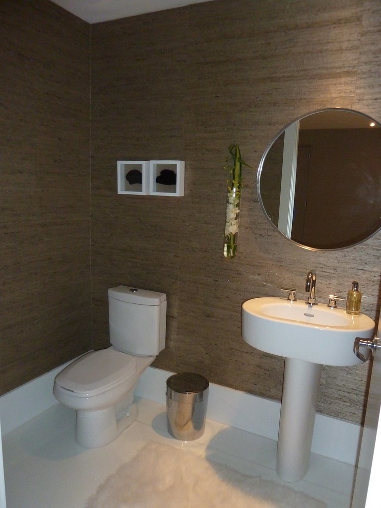 Elegant powder room with brown textured wallpaper, round mirror and pedestal sink