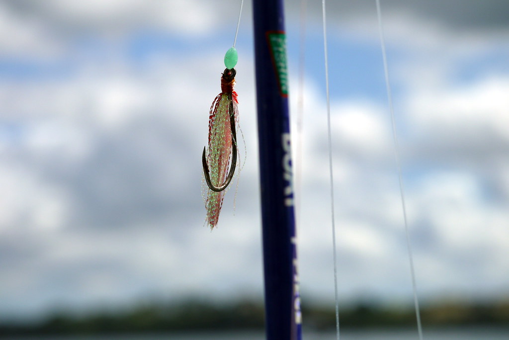 A feathered fishing lure with a bare hook dangling from a line against a cloudy sky, by Yortw, on Flickr