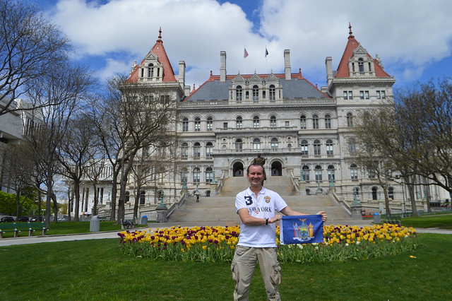 Ryan Janek Wolowski waving the state flag of New York at the The New York State Capitol building a National Historic Landmark on the Empire State Plaza in the capital city of Albany, NY, USA