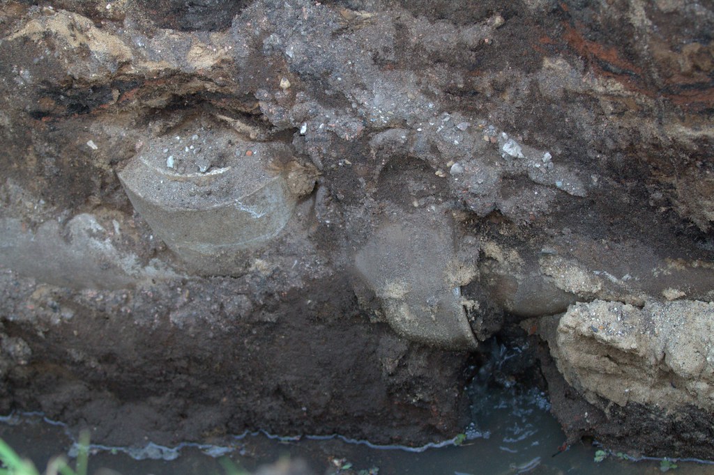 Broken underground pipe exposed in a muddy trench with standing water