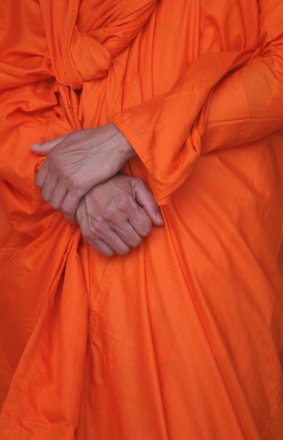 Hands clasped on Buddhist's orange robes Laos