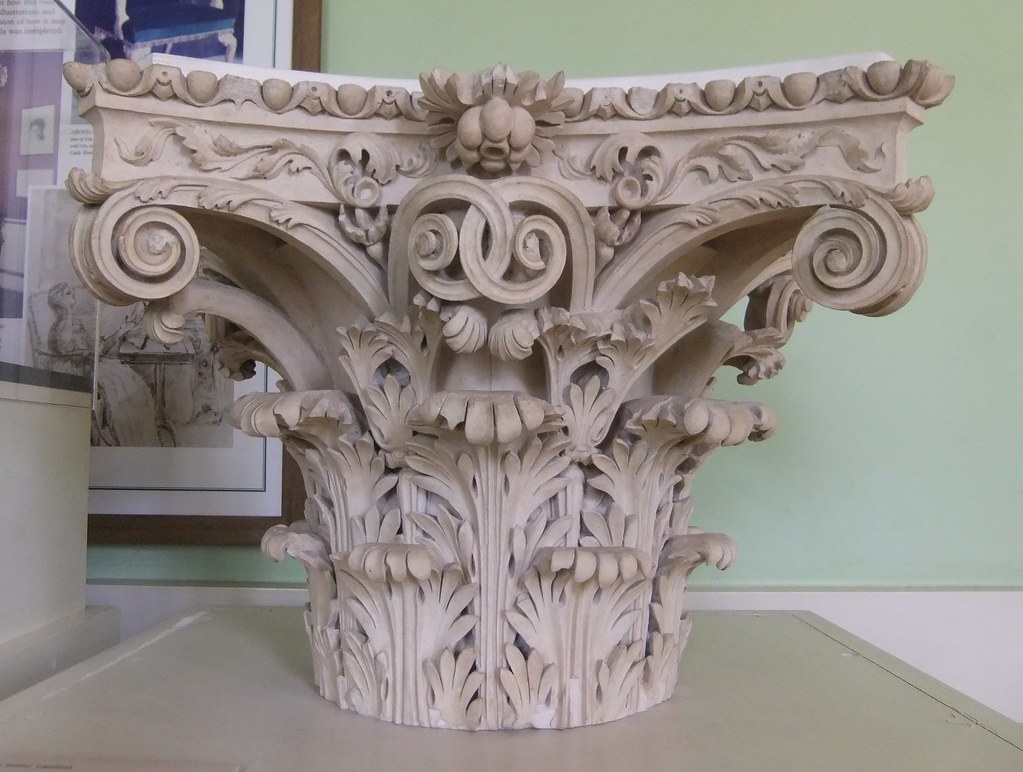 Corinthian capital depicted with ornate flutes and decorations in the shape of leaves. 