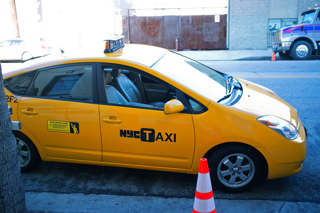 Bright yellow NYC Taxi Prius parked curbside with an orange cone in Downtown Los Angeles, California.