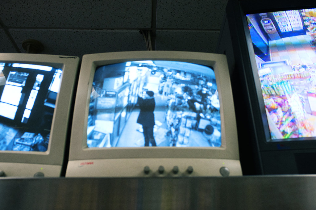 Surveillance monitor self-portrait showing the photographer holding a camera inside a grocery store.