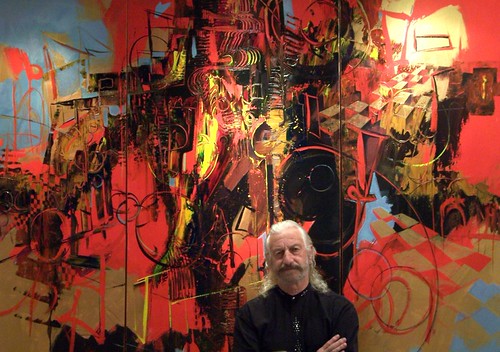 Artist standing beside a large red abstract painting