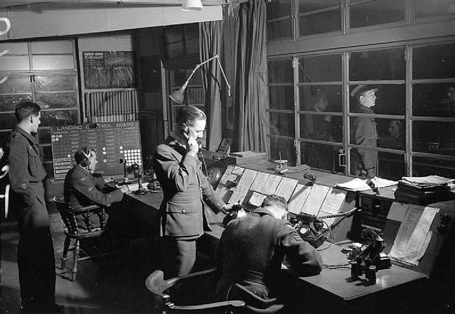 The Officer of the Watch in the Watch Office at Snaith, Yorkshire, guiding Handley Page Halifaxes of No. 51 Squadron RAF back to base after a night raid on Nuremberg. The Station Commander of Snaith, Group Captain N H Fresson, can be seen waiting outside