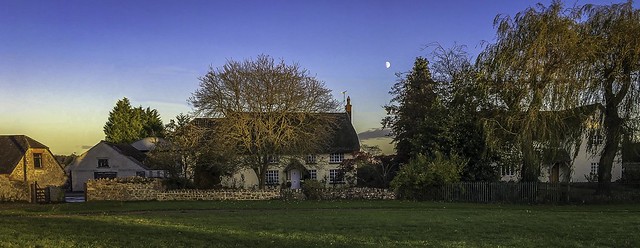 The moon rises behind houses on the village green at Poulshot in Wiltshire