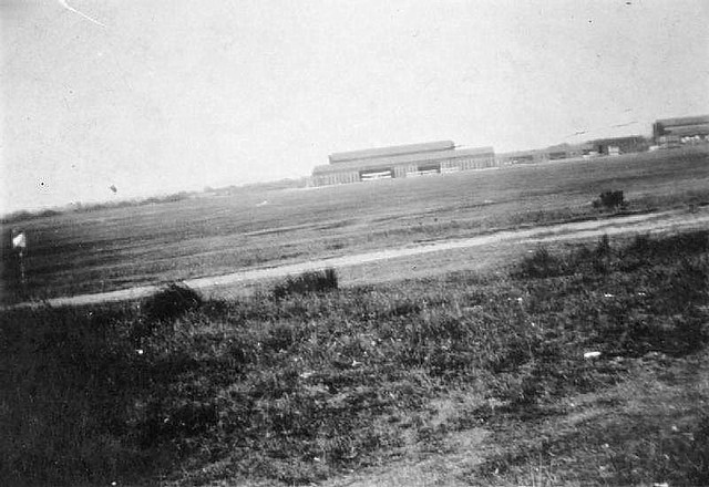 Farnborough - A long distance photograph of the Royal Aircraft Establishment hangars. A biplane can be seen in the entrance to one of the hangars. The image is rather over exposed.