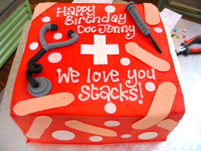 Square Wicked Chocolate cake iced in red butter icing decorated with fondant stethoscope, syringe, plasters & piped message