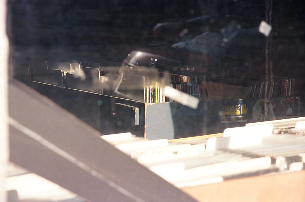 Rows of vinyl records in wooden crates seen through the reflective window of a record store.