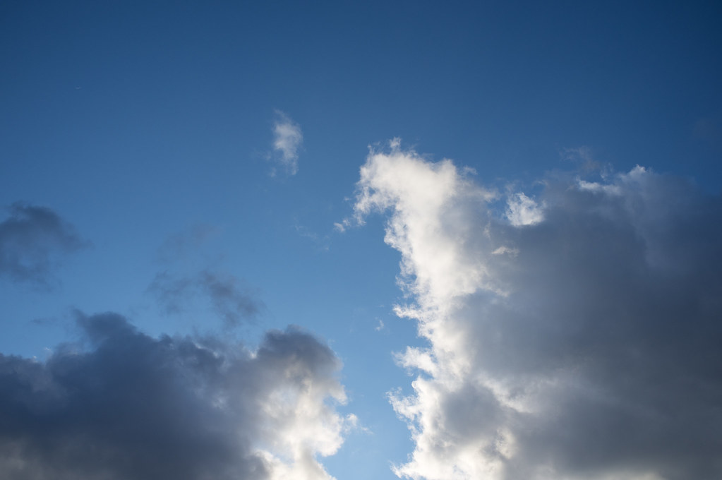 Dramatic billowing white and grey cumulus storm clouds backlit by sunlight against a deep blue sky.