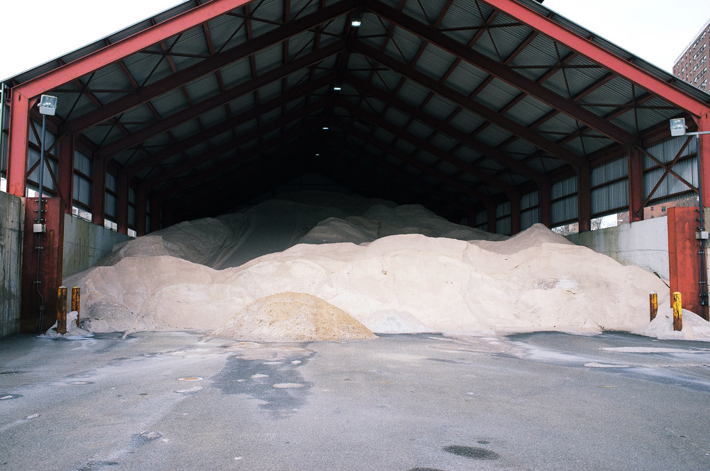Massive mounds of road salt stored inside a large open-front industrial red steel-frame barn shed.