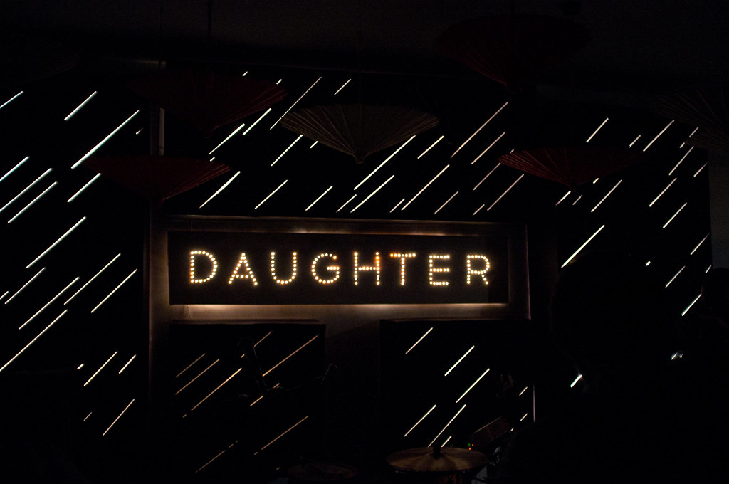 Stage marquee sign spelling 'DAUGHTER' in glowing incandescent bulbs against a dark slit backdrop.