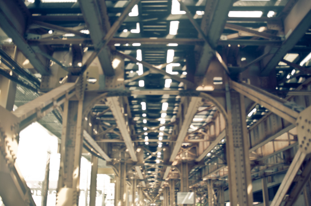 Looking up through steel beams and railroad ties beneath an elevated train track in Chicago.