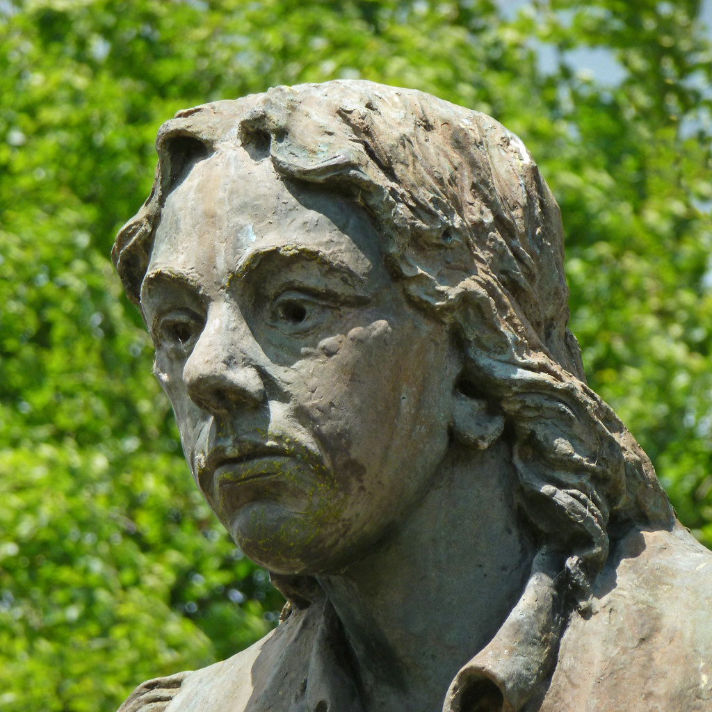 A weathered, outdoor statue of Thomas Chippendale. In the photo his face can be seen and he has long hair with distinct features. 