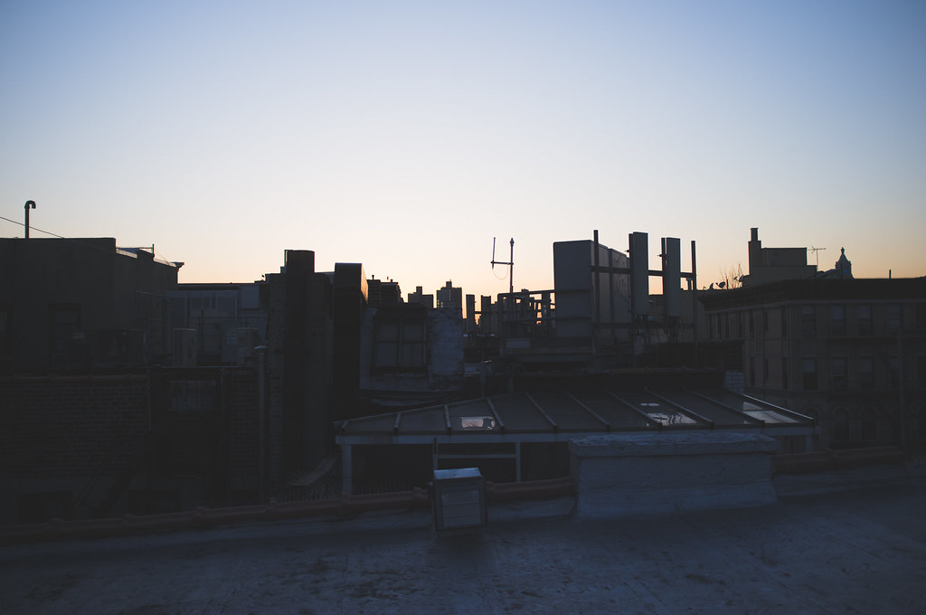 Silhouetted urban rooftop architecture, billboards, and antennas against a tranquil evening twilight sky.
