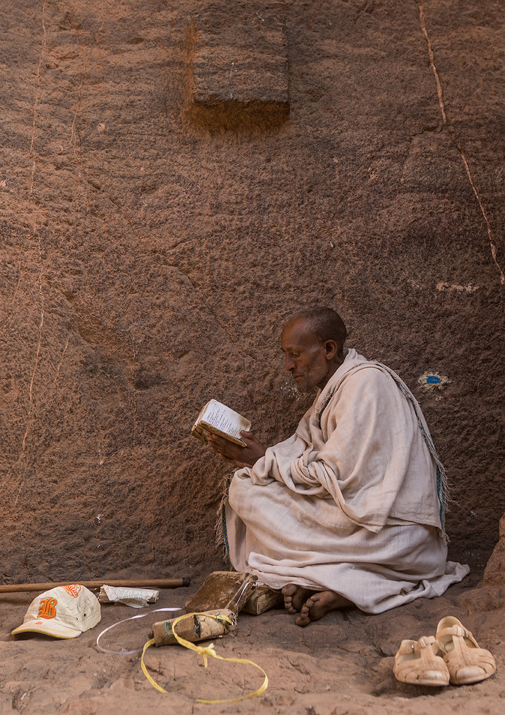 Lonely ethiopian orthodox man praying with a bible, Amhara region, Lalibela, Ethiopia