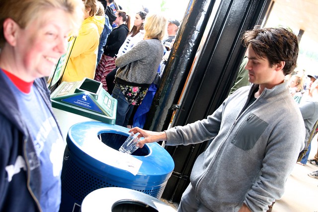 A man throwing a plastic bottle into the blue bin for recycling