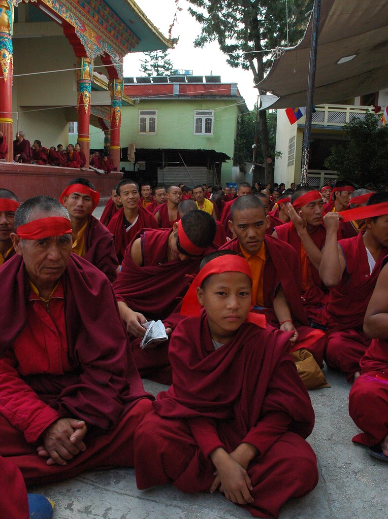 A composed young monk ready for initiation, Tibetan monks tying on red symbolic blindfolds for entry into the deity mandala, wearing traditional maroon garments, stage, Sakya Lamdre, Tharlam Monastery Courtyard, Boudha, Kathmandu, Nepal