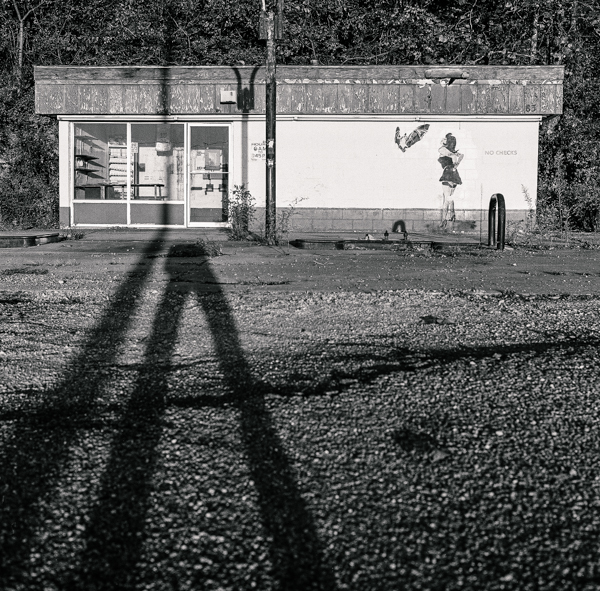 an abandonded gas station where shadows extend up a hill to touch the sky, and a graffiti artist has made a woman who whispers to a bat