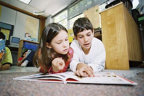 Two children reading a book on the floor.