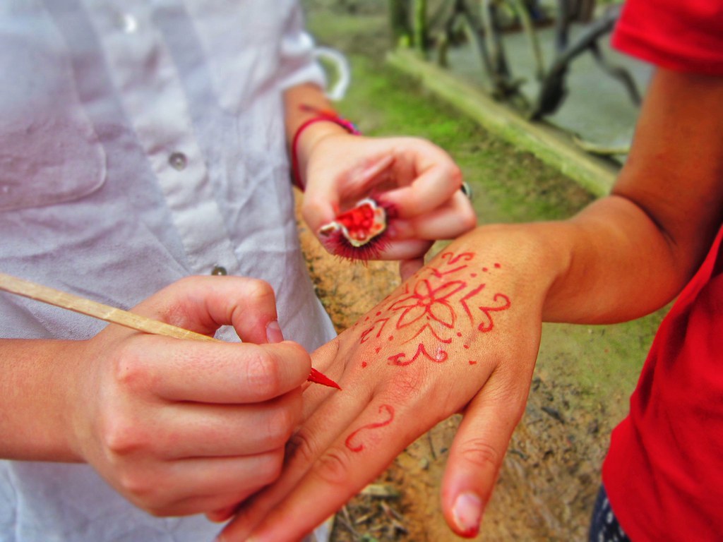 A hand painting red line designs on another hand in Misahualli, Ecuador
