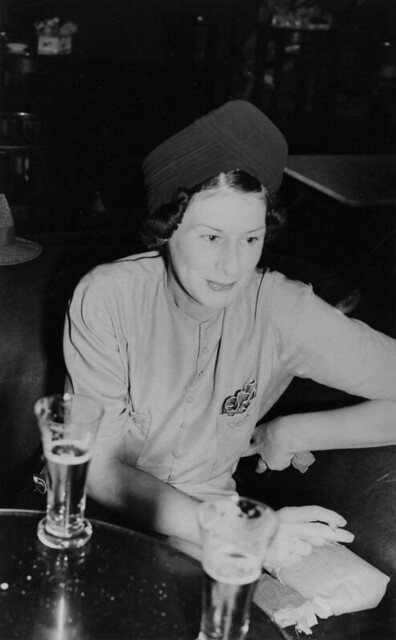 Woman with a cigarette sitting at a table at a bar having drinks, ca. 1940s