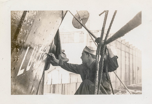 Sailor painting the name on the side of a ship
