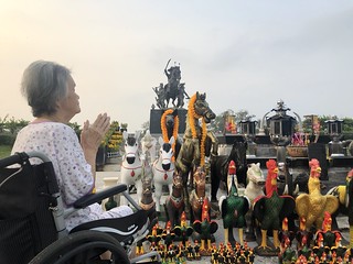 A senior woman on a wheelchair press the hands together at her chest in sign of respect in sign of respect the monument of the Great King Taksin Maharat of Thonburi Reign, Chanthaburi.