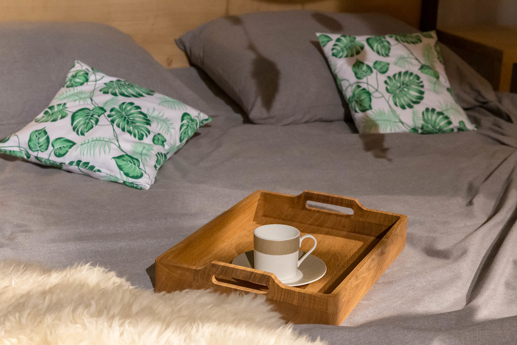Kaffeetasse für Frühstückskaffee auf Holztablett steht auf Bett mit bunten Kissen und Fell