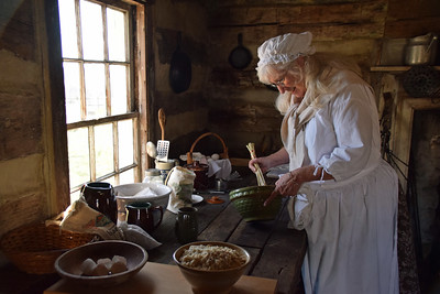 Women dressed in white colonial clothing mixes ingredients in a bowl. 