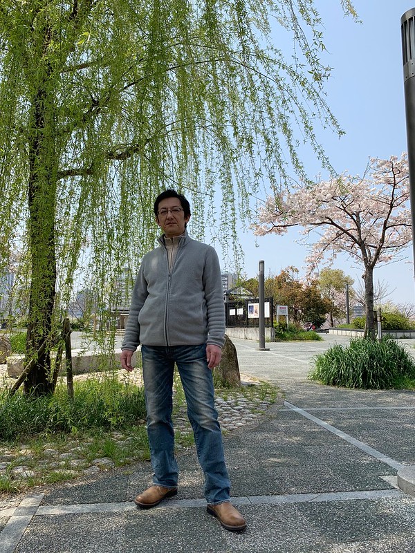 2019年4月6日、桜と柳を背景に、妻に撮影してもらった写真です。大阪市都島区の蕪村公園にて。リーバイスの502号のジーンズをはいています。